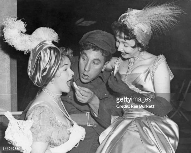 English actor and comedian Frankie Howerd helps to make up actresses Peggy Cummins and Dulcie Gray during rehearsals for the Royal Variety...