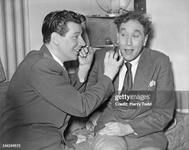 English entertainer Max Bygraves and actor and comedian Frankie Howerd helping each other with their make-up, backstage during rehearsals for the...