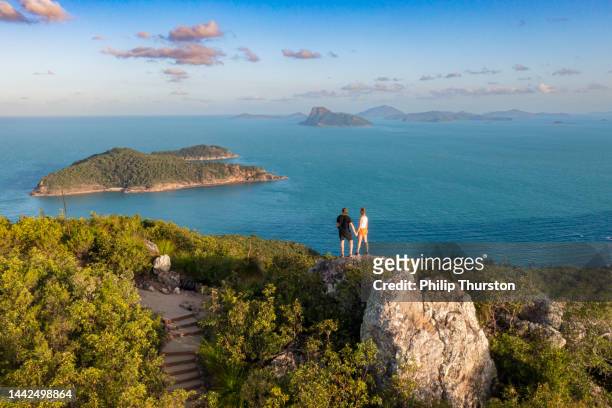 couple standing atop mountain overlooking deep blue ocean - hamilton island stockfoto's en -beelden