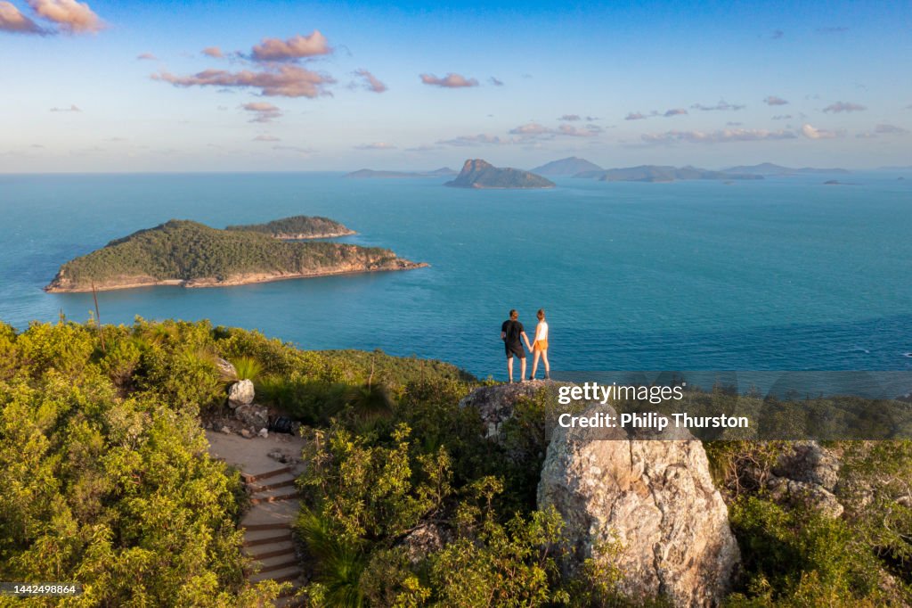 Couple Standing atop mountain overlooking deep blue ocean
