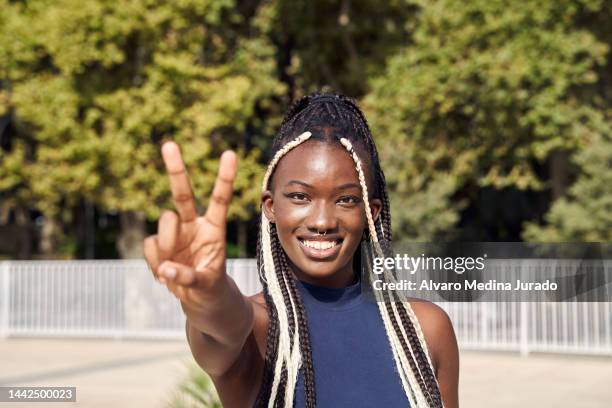 cheerful young african american girl outdoors in the city smiling and making v gesture with fingers of hand looking at camera. - victory sign stock-fotos und bilder