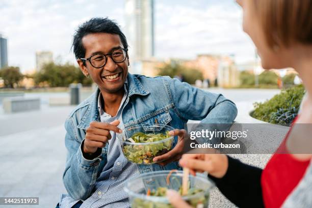 young couple eating a salad and talking on the bench in milan - eating salad stock pictures, royalty-free photos & images