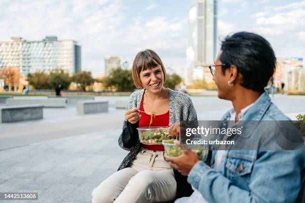 young couple eating a salad and talking on the bench in milan - salad to go stock pictures, royalty-free photos & images