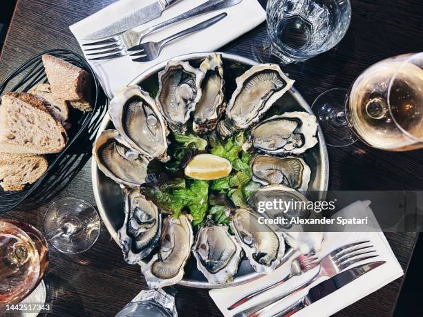 oysters plate and white wine in a restaurant, directly above view - oysters stock-fotos und bilder