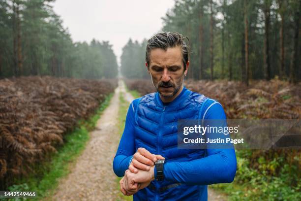 athletic male out for a run on a rainy day in the forest. he stops to check his smartwatch for his running data - extra portraits stockfoto's en -beelden