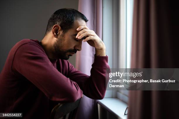 a stressed man holding his head with his hand, sitting by the window - hand on head stock-fotos und bilder