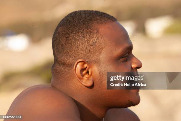 a happy handsome young man seen in profile, a smiling twenty something with a short shaved afro crew cut smiles as he's seen in profile looking away from camera - shaved head profile stock pictures, royalty-free photos & images