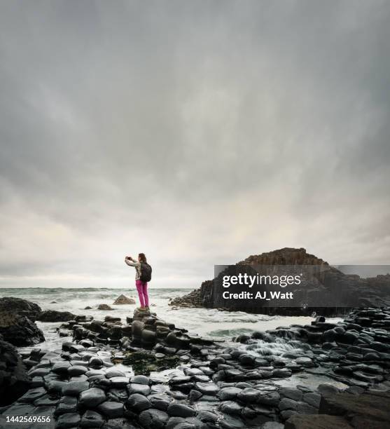 woman taking photos during a hike by the giants causeway - giants causeway stock pictures, royalty-free photos & images