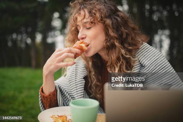 woman enjoys eating a croissant while telecommuting and camping - eating croissant stock pictures, royalty-free photos & images