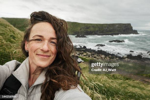 frau lächelt und macht selfies während einer küstenwanderung - giants causeway stock-fotos und bilder