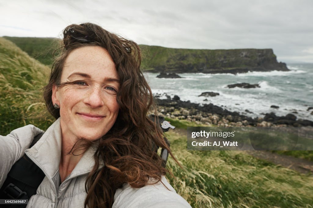 Woman smiling and taking selfies during a coastal hike