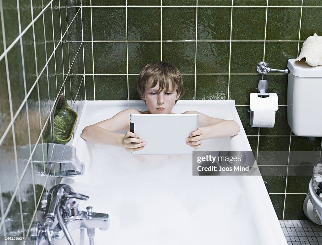 Boy in a bubble bath using digital tablet