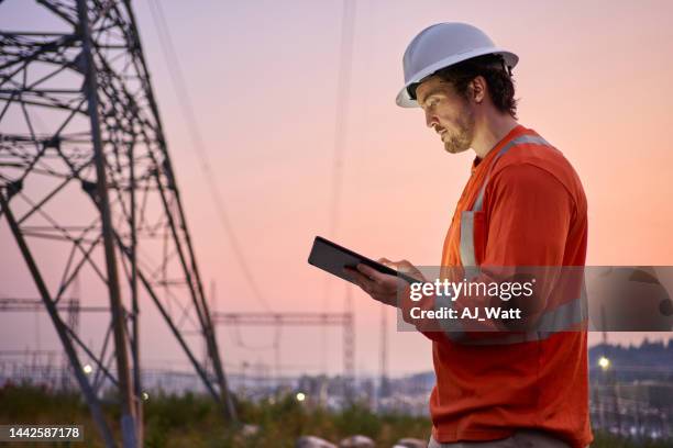 electrical engineer using a tablet by pylons at dusk - technician stock pictures, royalty-free photos & images