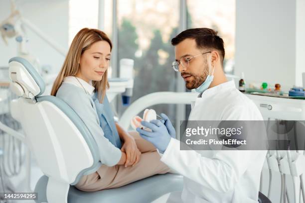 dentist showing jaw model to female patient - human jaw bone stockfoto's en -beelden
