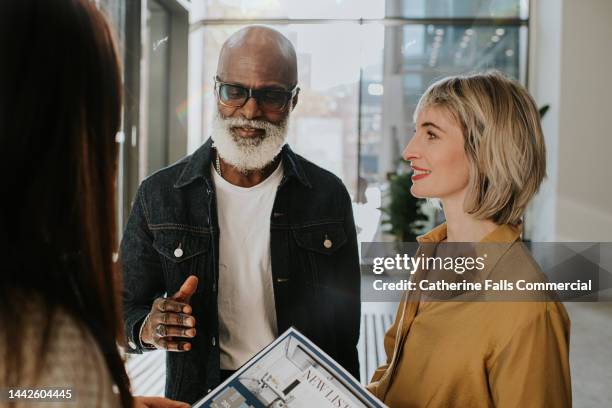two smartly dressed people stand in front of an estate agent. the man talks as the two woman listen. - commercial real estate agent stock pictures, royalty-free photos & images