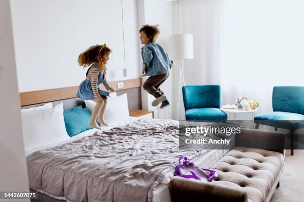 hermano y hermana jugando y saltando en la cama de la habitación del hotel - a boy jumping on a bed fotografías e imágenes de stock