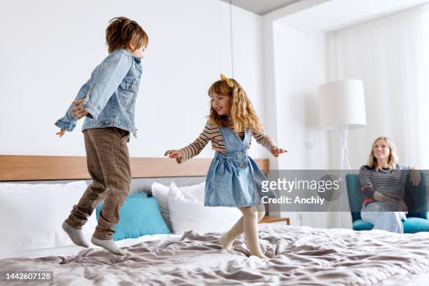 bruder und schwester spielen und springen auf dem bett im hotelzimmer - couple playful bedroom stock-fotos und bilder