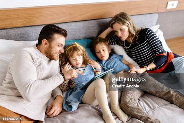 family laying on bed in a hotel room watching digital tablet - guest room stock pictures, royalty-free photos & images