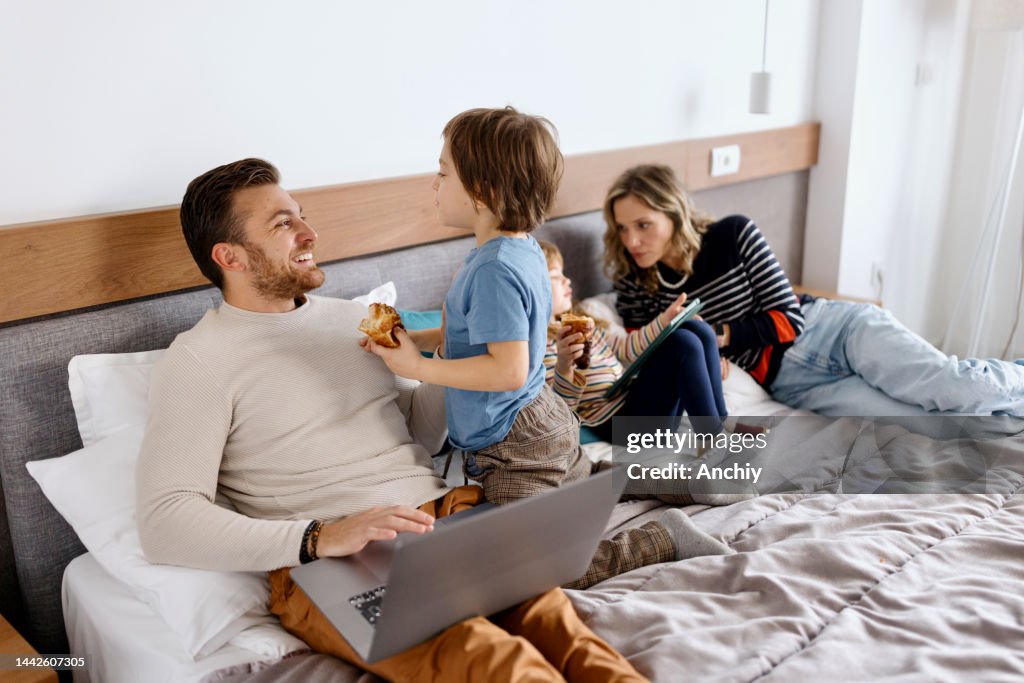 A father is using a laptop while his son interrupts him while he is working