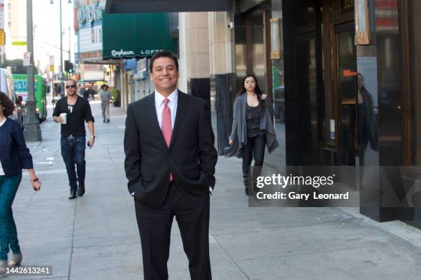 On Broadway with the Orpheum Theatre behind him Council Member José Huizar wearing a suit and tie and smiling poses with his hands in his pockets for...