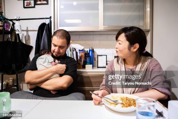 a father holding his sleeping newborn daughter in his arms and a mother smiling and eating curry next to him. - yōshoku stock pictures, royalty-free photos & images
