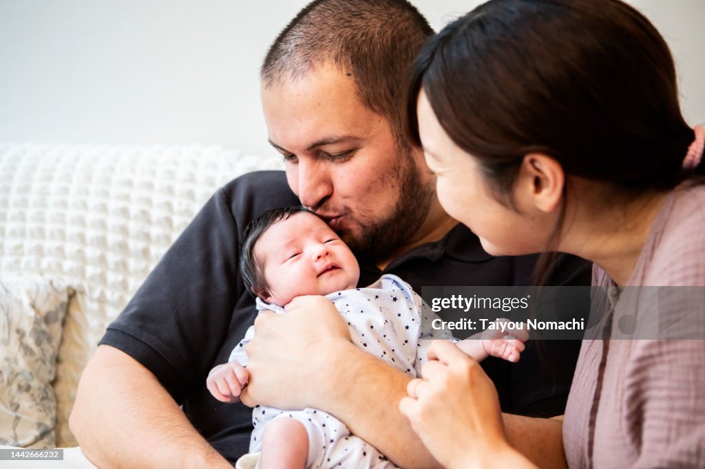 A father kisses his newborn daughter and a mother watches by his side.