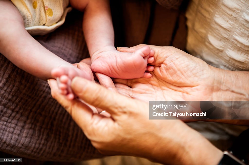 Close-up of newborn baby's feet and grandmother's hands.