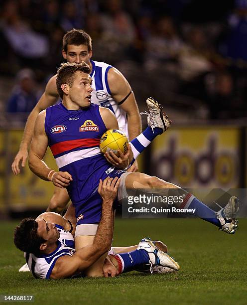 Shaun Higgins of the Bulldogs handballs whilst being tackled by Michael Firrito of the Kangaroos during the round seven AFL match between the North...