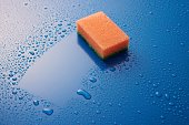 Orange double sided cleaning sponge paled on blue background covered with drops with copyspace