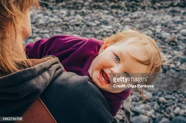 cheerful infant child looks over shoulder of a parent and laughs - intergénero fotografías e imágenes de stock