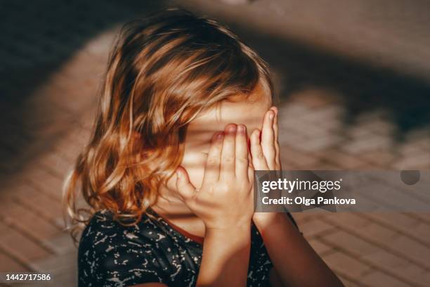 preschool child covers his face with his hands - shy stock-fotos und bilder