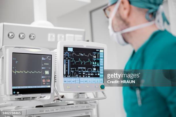 männlicher chirurg untersucht pulsspur auf monitoren während der operation - anesthesiologist stock-fotos und bilder