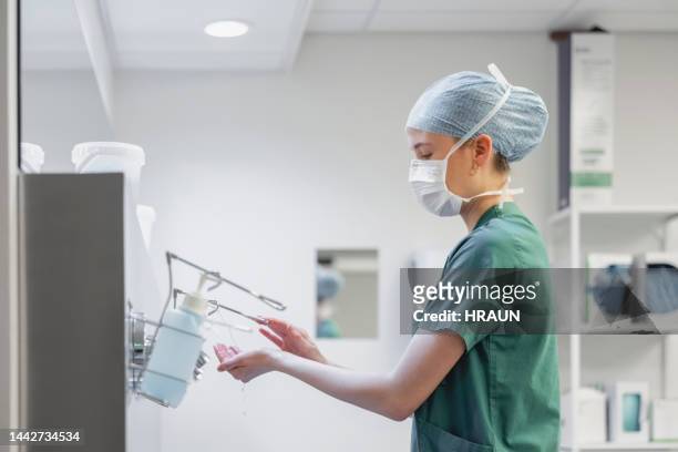 female nurse in surgical mask and cap using hand sanitizer in operation room - desinfetar imagens e fotografias de stock
