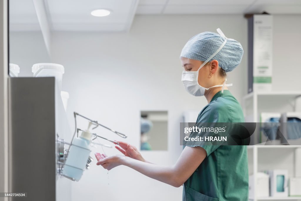 Female nurse in surgical mask and cap using hand sanitizer in operation room