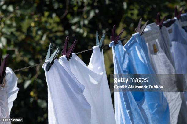 clean sweaters, trousers and t-shirts hang on a rope outside on a sunny summer day. washed women's, men's and children's clothes, bed linen are dried on a clothesline, a clothes dryer. the concept of homework, household duties. non-urban scene. - women in wet tee shirts stock pictures, royalty-free photos & images