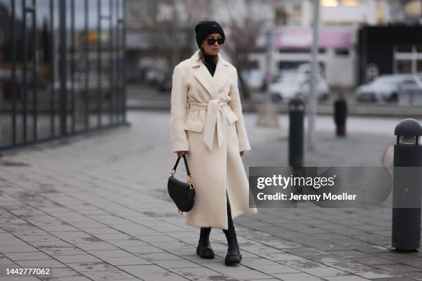 Benthe Liem is seen wearing creme white Almada long coat, black Ray Ban sunglasses, Dior black leather saddle bag and Copenhagen Studios CPH143...