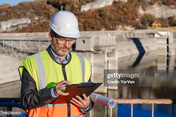 male engineer working writing on a clipboard in hydroelectric dam - reservoir engineering stock pictures, royalty-free photos & images