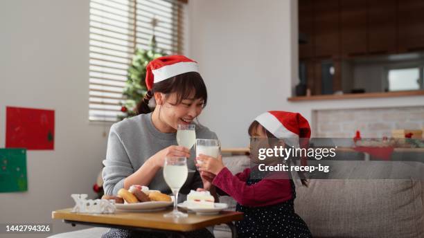 母親と小さな就学前の娘は、自宅のリビングルームのソファに座ってリラックスしながら、クリスマスケーキを食べたり飲み物を飲んだりしています - christmas cake ストックフォトと画像