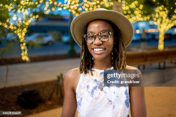 elegante afroamerikanische frau in ihren zwanzigern in einem park in el paso texas unter dekorativer beleuchtung bei der interaktion auf einem laptop während einer telefonkonferenz - businesswoman under stock-fotos und bilder