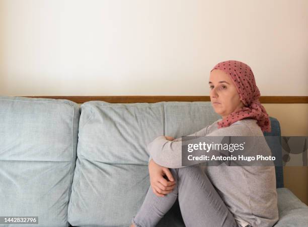 portrait of a woman with cancer and depression locked in her home thinking. sitting on the sofa. pink headscarf. quarantine coronavirus. - hospital quarantine stock pictures, royalty-free photos & images