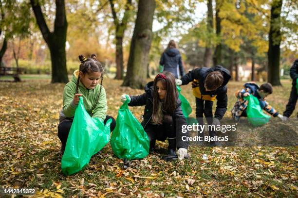 kids collecting garbage in garbage bag while cleaning public park - earth day stock pictures, royalty-free photos & images