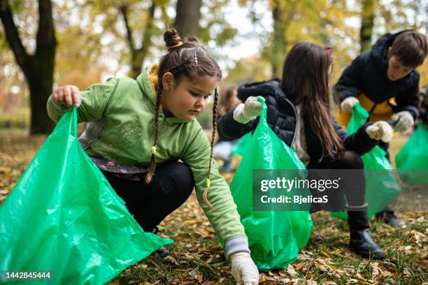 kinder sammeln müll im müllsack, während sie den öffentlichen park reinigen - combine day 6 stock-fotos und bilder