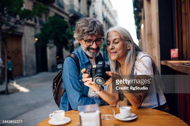 mature couple on vacation enjoying at the cafe and watching their photos - barcelona cafe stock pictures, royalty-free photos & images