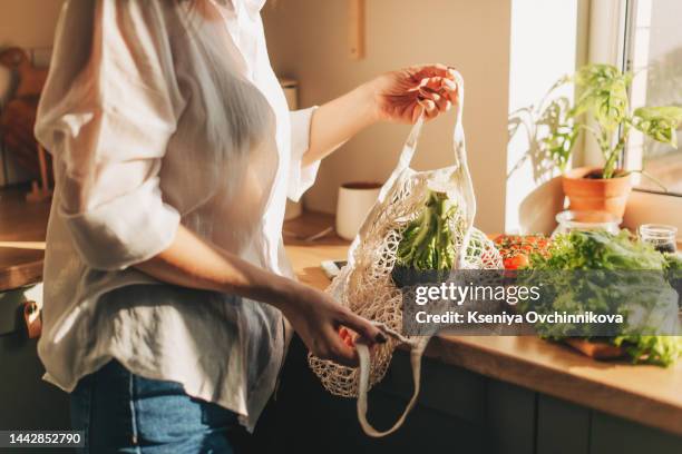 shopping bag with raw vegetables and fruits held by young woman in casualwear - ama de casa comprando fotografías e imágenes de stock