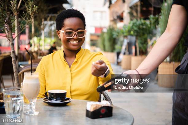 young african woman using her smartwatch to make a payment at the cafe - smart watch stock pictures, royalty-free photos & images