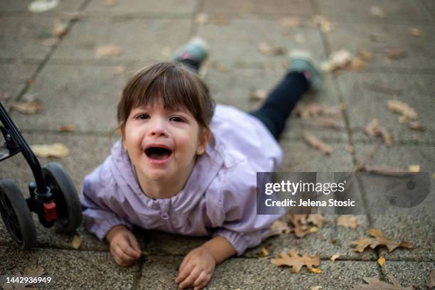 a little girl is lying on the ground in a public park and crying. - toddler tantrum stock pictures, royalty-free photos & images