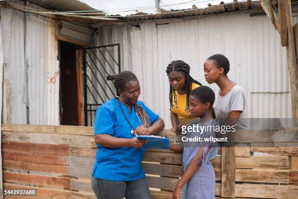 community nurse talking to teenage girls in an informal settlement infront of a shack - village life stockfoto's en -beelden