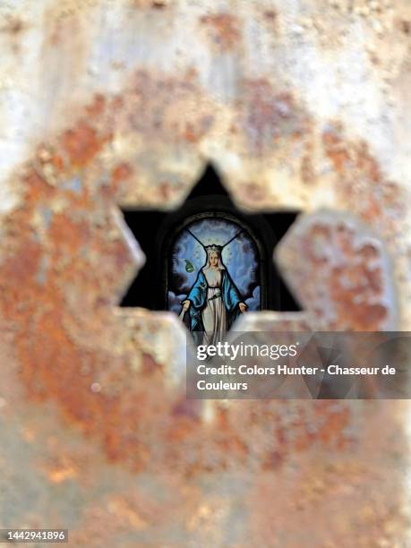 the virgin mary on a stained glass window seen through a star cut in a weathered metal door in paris - church color light paris stockfoto's en -beelden