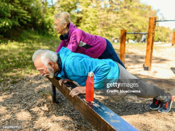 senior-paar streckt sich nach dem joggen in einem öffentlichen park. - liegestütze stock-fotos und bilder