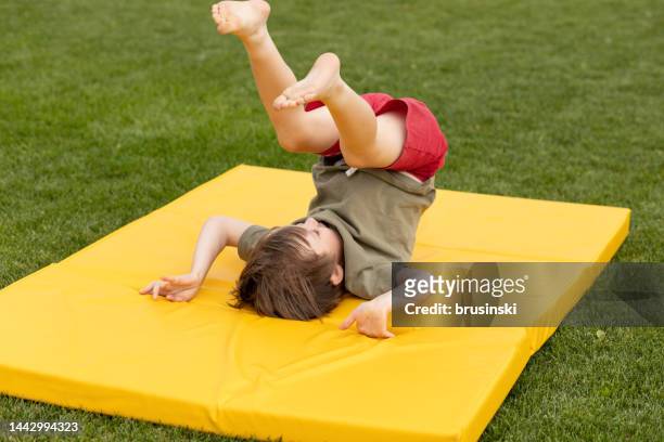 menino branco alegre de 5 anos fazendo exercícios de ginástica em um tapete macio no quintal de sua casa - somersault - fotografias e filmes do acervo
